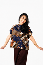 Woman wearing a patterned top and brown pants on a white background