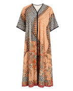 A long kaftan-style dress with a complex patchwork print, featuring a peach and orange floral pattern mixed with gray and black geometric and floral panels, finished with a red polka-dot hem.