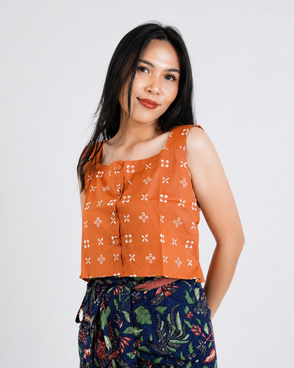Woman wearing an orange patterned top with a plain background
