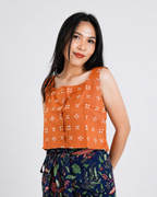 Woman wearing an orange patterned top with a plain background