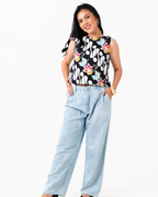 Woman wearing a sleeveless floral top and light blue pants on a white background