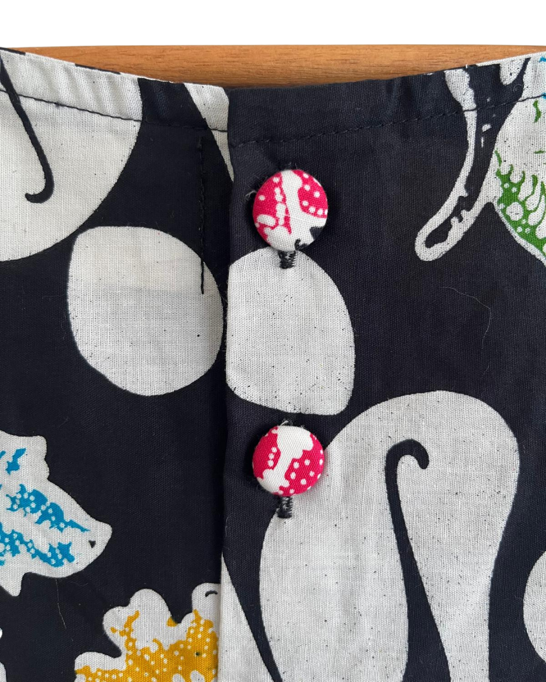 Close-up of a button on a fabric with a pattern of abstract shapes and a wooden surface at the top.