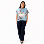 Woman wearing a colorful patterned top and dark pants on a white background